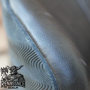 May include: Close-up of a black leather chair with a textured surface and a black, textured, curved edge. The chair is part of a set of furniture.