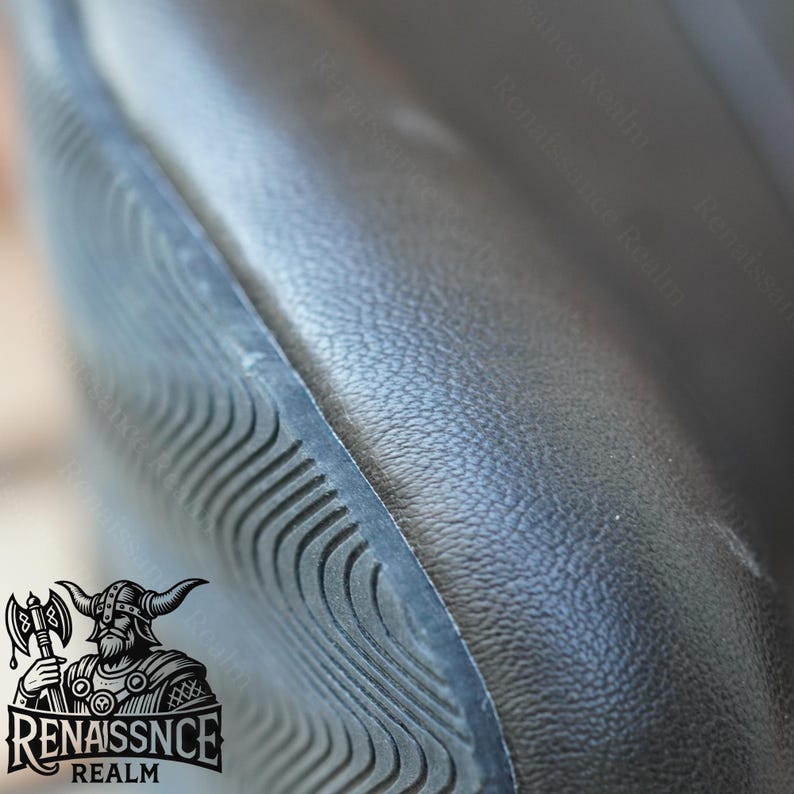 May include: Close-up of a black leather chair with a textured surface and a black, textured, curved edge. The chair is part of a set of furniture.