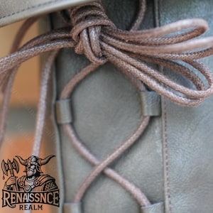 May include: Close-up of a brown leather boot with a brown lace-up closure. The laces are tied in a knot at the top of the boot.
