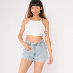 Puede incluir: Un short vaquero azul claro con bordes deshilachados y cintura alta. El short lo lleva puesto una persona con las piernas y los pies descalzos.