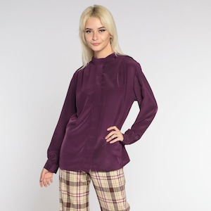 May include: A woman wearing a purple long-sleeved blouse and plaid trousers. The trousers have a wide leg and are a beige and brown plaid.