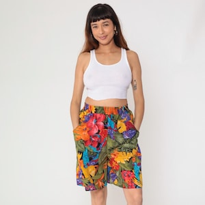 May include: A white tank top paired with colorful floral print shorts. The shorts feature a vibrant pattern of red, orange, yellow, and blue flowers with green leaves. The shorts have pockets and an elastic waistband.