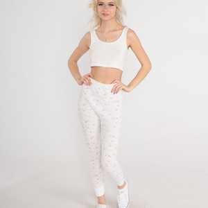 May include: A woman wearing a white tank top and white floral print leggings with white sneakers.
