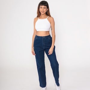 K&ouml;nnte beinhalten: Ein wei&szlig;es Neckholder-Top und dunkelblaue Jeans. Die Jeans haben eine hohe Taille und eine gerade Beinpassform. Das Model tr&auml;gt wei&szlig;e Turnschuhe.