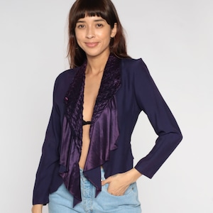 Puede incluir: Una chaqueta azul marino con un cuello de satén y terciopelo morado. El cuello es fruncido y asimétrico.