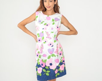 Puede incluir: Vestido blanco sin mangas con un vibrante estampado floral en rosa, morado y verde. El vestido presenta una silueta recta y un dobladillo azul marino. El diseño floral incluye grandes flores y flores más pequeñas.
