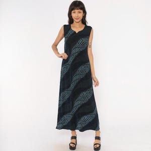 Pode incluir: Um vestido comprido sem mangas na cor preta com um padrão ondulado repetitivo de pequenas formas de folhas azuis. A peça tem um decote redondo simples e uma silhueta reta e fluida que se estende até aos tornozelos.