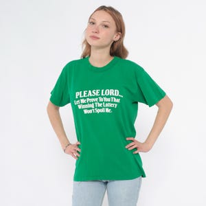 K&ouml;nnte beinhalten: Ein gr&uuml;nes T-Shirt mit dem Text "PLEASE LORD... Let Me Prove To You That Winning The Lottery Won't Spoil Me." in Wei&szlig;. Das Shirt hat einen Rundhalsausschnitt.