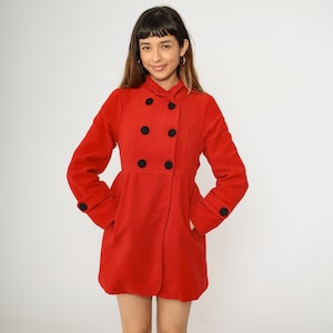 May include: A vibrant red coat with a double-breasted design. It has large black buttons, a flared skirt, and pockets. The sleeves have black button details at the cuffs. A classic coat style.