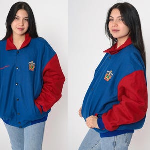 May include: A blue and red varsity jacket with a logo on the left side. The jacket has a snap closure and a ribbed collar, cuffs, and hem.