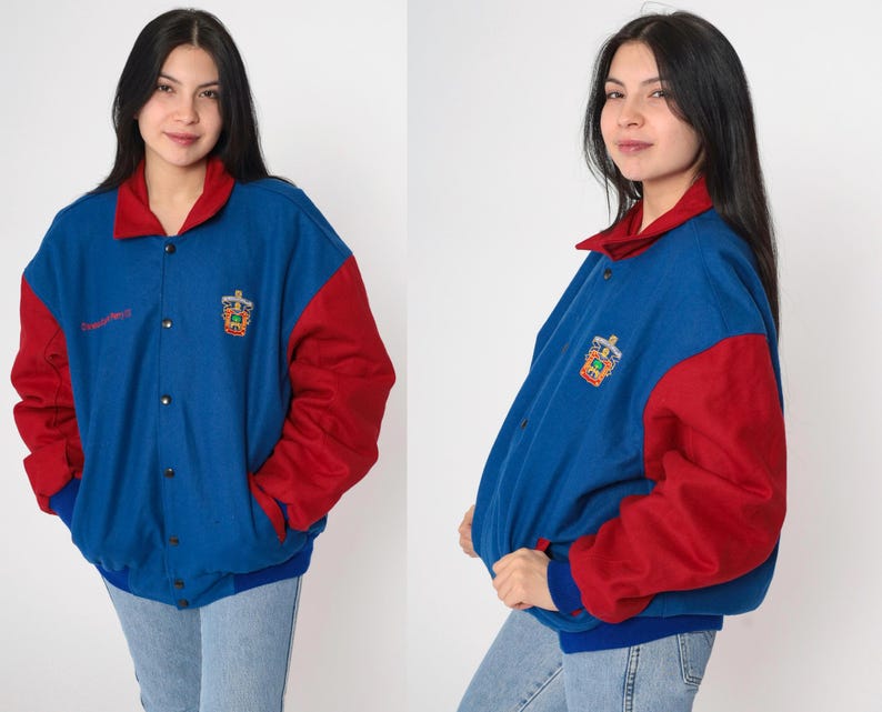 May include: A blue and red varsity jacket with a logo on the left side. The jacket has a snap closure and a ribbed collar, cuffs, and hem.