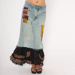 May include: Light blue denim skirt with colourful patchwork details. The skirt features a tiered black ruffle hem with floral fabric accents. The skirt is worn with black platform sandals.
