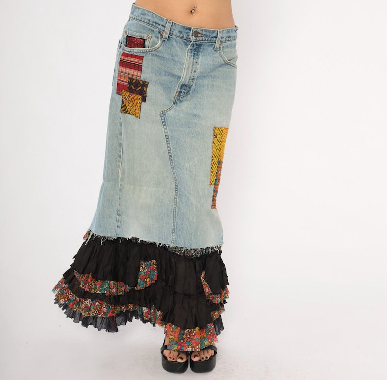 May include: Light blue denim skirt with colourful patchwork details. The skirt features a tiered black ruffle hem with floral fabric accents. The skirt is worn with black platform sandals.