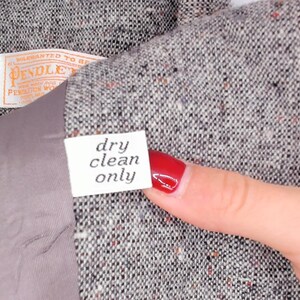 May include: Close-up of a gray tweed jacket with a label that reads "dry clean only." The jacket has a gray lining and a Pendleton label. The fabric has flecks of red and orange.