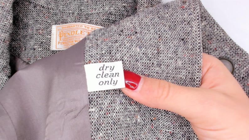 May include: Close-up of a gray tweed jacket with a label that reads "dry clean only." The jacket has a gray lining and a Pendleton label. The fabric has flecks of red and orange.