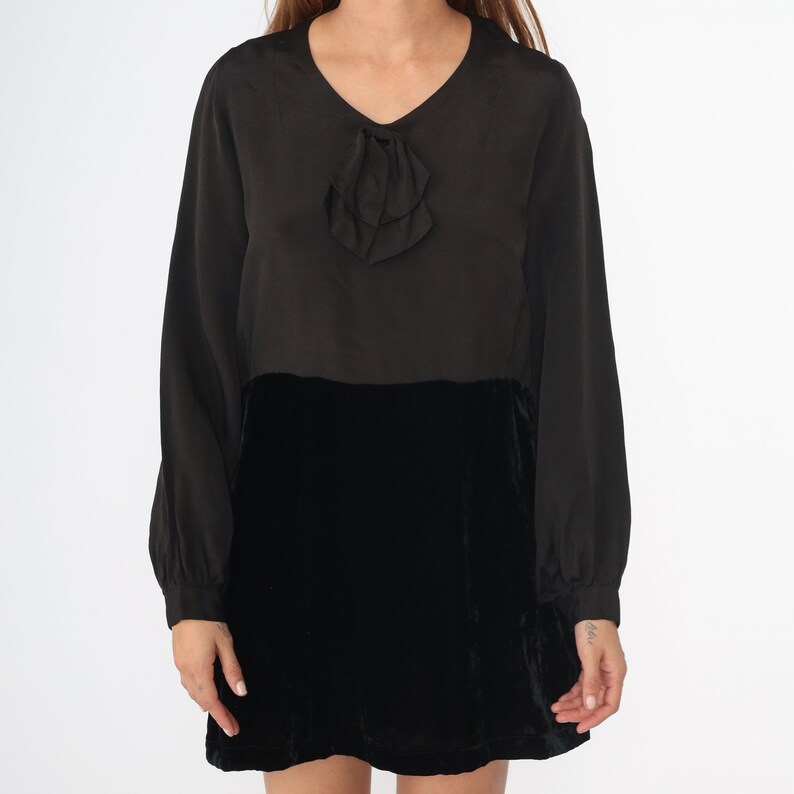 May include: A black long-sleeved dress with a velvet skirt and a ruffled bow detail at the neckline.