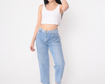 May include: A woman wearing a white tank top and light blue denim jeans. She is standing with her arms at her sides and her hair is pulled back.