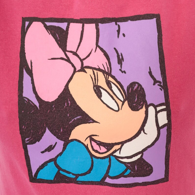 May include: A bright pink fabric featuring a square graphic print of Minnie Mouse. The character is depicted in profile with a large pink bow, a blue dress, and white gloves, set against a light purple background with a thick, dark, hand-drawn style border.