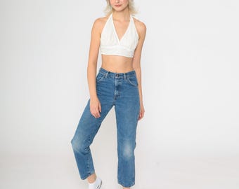 May include: A white halter top with a v-neckline and a blue denim pair of high-waisted jeans.