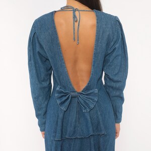 Puede incluir: Un vestido de mezclilla azul de manga larga con un dise&ntilde;o de espalda abierta profunda. La prenda incluye un cierre de lazo en la nuca y un detalle de lazo decorativo de mezclilla en la parte baja de la espalda, sobre una cremallera vertical.