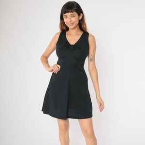 Pode incluir: Um vestido preto sem mangas com um detalhe de laço no decote. O vestido tem um corpete justo e uma saia rodada.