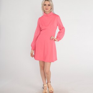 May include: A pink dress with a high neck and long sleeves. The sleeves are made of a sheer fabric with a geometric pattern. The dress has a fitted bodice and a flared skirt.