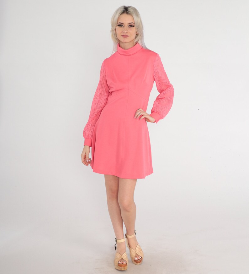 May include: A pink dress with a high neck and long sleeves. The sleeves are made of a sheer fabric with a geometric pattern. The dress has a fitted bodice and a flared skirt.