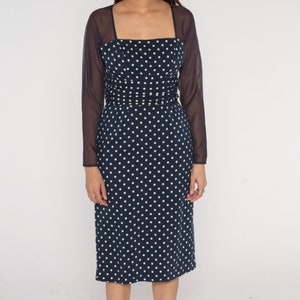 May include: A navy blue dress with white polka dots and a matching sheer overlay. The dress has a square neckline and a fitted silhouette.