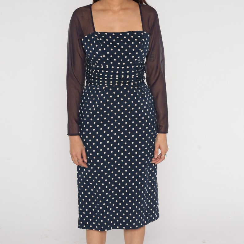 May include: A navy blue dress with white polka dots and a matching sheer overlay. The dress has a square neckline and a fitted silhouette.