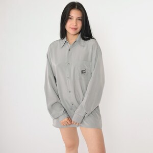 May include: A gray long-sleeved button-down shirt with a small alligator logo embroidered on the left chest pocket.