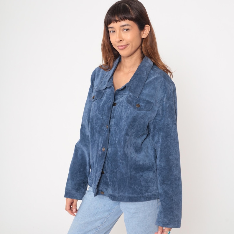 May include: A blue corduroy jacket with a button-up front, two chest pockets, and a collared neckline. The jacket is a solid blue color and appears to be made of a soft, textured fabric. The jacket is worn with light blue jeans.