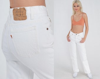 May include: White denim jeans with a high waist and a straight leg. The jeans have a small brown leather patch on the back waistband.