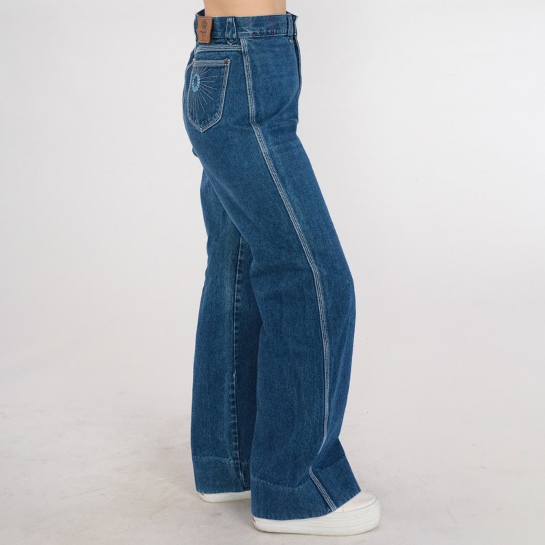 May include: A pair of blue denim wide-leg jeans with a decorative embroidered design on the back pocket.