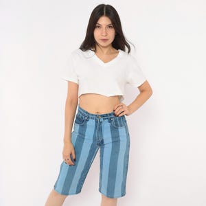 May include: A white short-sleeved v-neck crop top paired with knee-length denim shorts featuring vertical stripes in alternating shades of light blue and medium blue, complete with a standard button fly and five-pocket construction.
