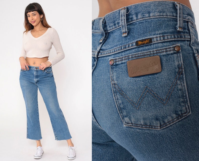 May include: A pair of light blue denim jeans with a brown leather patch that says "Wrangler" on the back pocket. The jeans have a straight leg and a frayed hem.