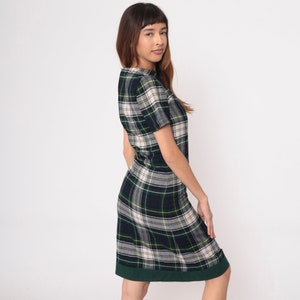 May include: A plaid dress in a green, navy, and cream pattern. The dress has short sleeves and a knee-length hem with a dark green border. The fabric has a classic tartan design, suitable for casual wear.