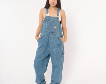 May include: Light blue denim overalls featuring a bib pocket with a button closure, two side pockets, and adjustable shoulder straps with metal hardware. The garment has a loose, relaxed fit with straight legs and a classic medium wash finish.