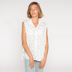 May include: White sleeveless button-down shirt with a colorful leaf pattern. The shirt features a collared neckline and a relaxed fit. The pattern includes red, yellow, blue, and green leaf shapes.