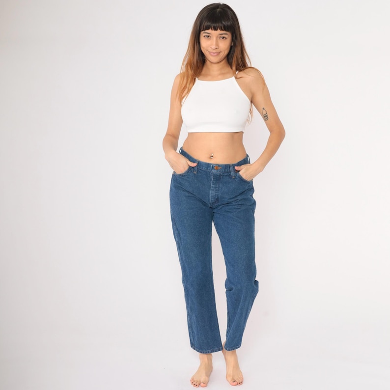 May include: A woman wearing a white crop top and blue denim jeans. The jeans have a high waist and a straight leg.