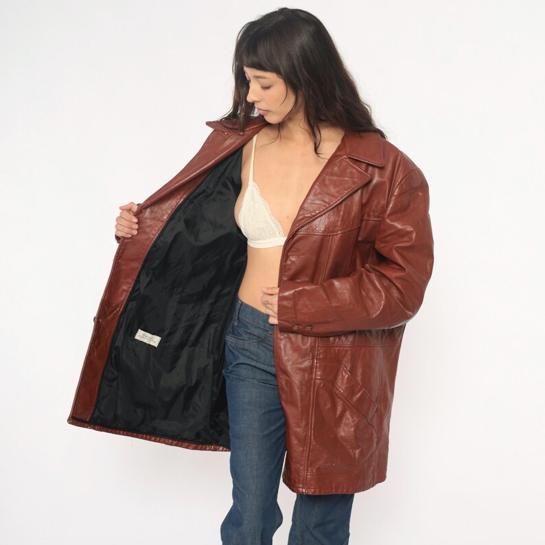 May include: A brown leather coat with a classic lapel collar and a button closure. The coat has a tailored fit and a black interior lining. The coat is knee-length and has a vintage aesthetic.