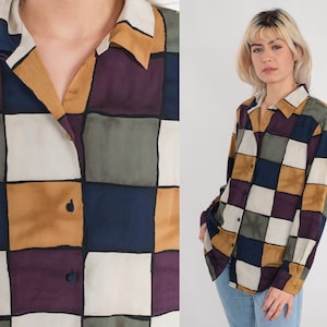 May include: A button-down shirt with a checkerboard pattern in shades of white, navy, mustard yellow, olive green, and purple. The shirt has a collared neckline and long sleeves. The squares are outlined in black.