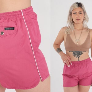 May include: Pink athletic shorts with white trim along the side seams. The shorts feature an elasticated waistband and a small pocket on the back with a black label that says "Zippo".