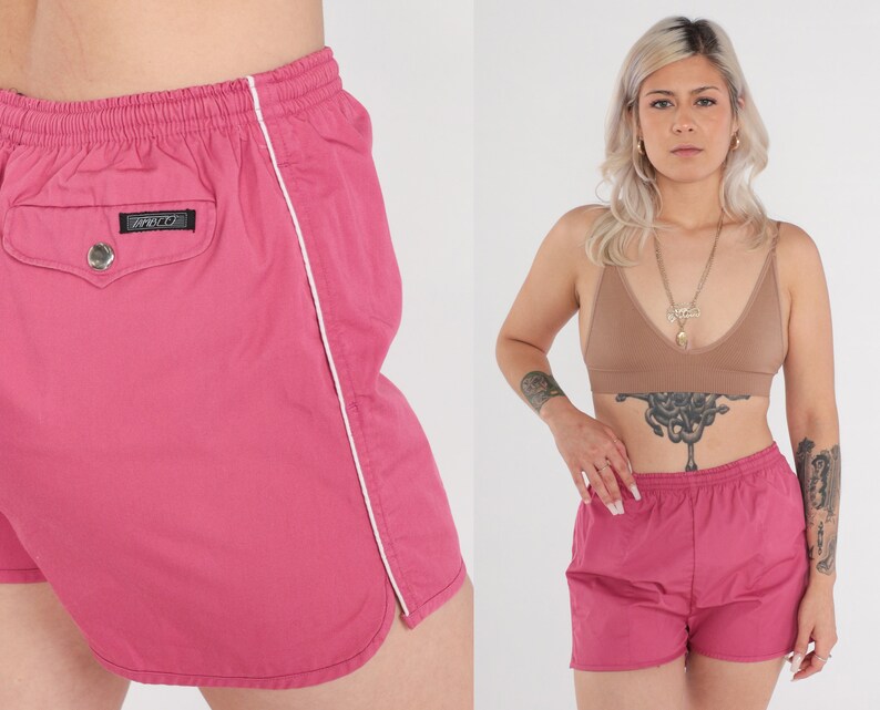 May include: Pink athletic shorts with white trim along the side seams. The shorts feature an elasticated waistband and a small pocket on the back with a black label that says "Zippo".