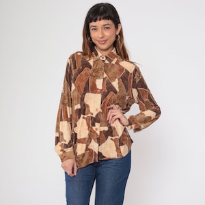 May include: A long-sleeved button-down shirt with a patchwork design in shades of brown and beige. The shirt has a collared neckline and buttoned cuffs. The shirt is paired with blue jeans.