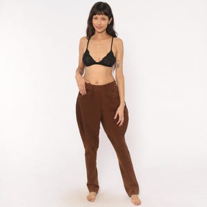 May include: A black lace bralette with thin straps and a scalloped edge paired with high-waisted brown trousers featuring a wide hip design, a button closure, and a tapered leg silhouette that extends down to the ankles in a solid matte finish.