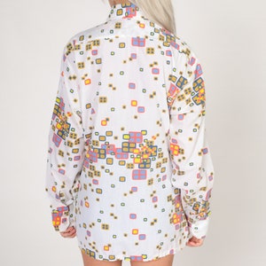 May include: White long-sleeved shirt with a geometric pattern in shades of blue, red, yellow, and brown.