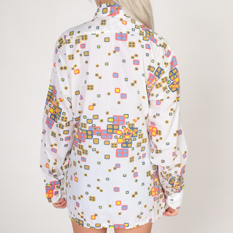 May include: White long-sleeved shirt with a geometric pattern in shades of blue, red, yellow, and brown.