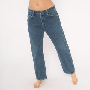 May include: Blue denim jeans with a classic five-pocket design. The jeans have a straight leg cut and a button and zipper closure. The denim is a medium wash, and the jeans appear to be unworn.