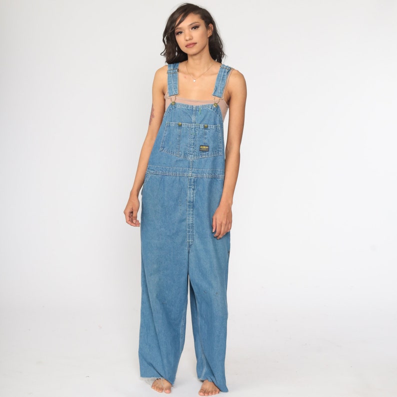 May include: Light blue denim dungarees with a wide leg and adjustable straps. The dungarees have a single front pocket and a brand label on the right hip.
