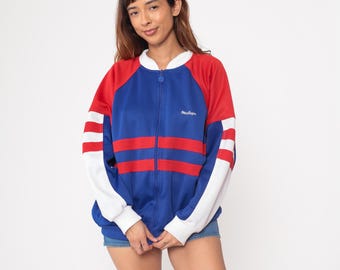 May include: A zip-up track jacket in red, white, and blue. The jacket has a blue center panel with two red stripes across the chest. The sleeves are red with white stripes. The jacket has a white collar and cuffs. The text "Retro Sport" is embroidered on the chest.